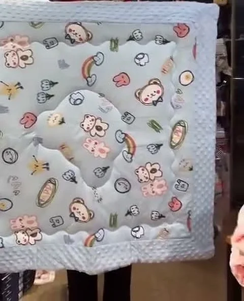 A pastel blue muslin baby blanket with a cartoon bear, rainbow and cloud print.