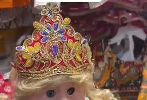 A baby doll modelling the companion Radha costume, with a blonde wig and a matching crown.